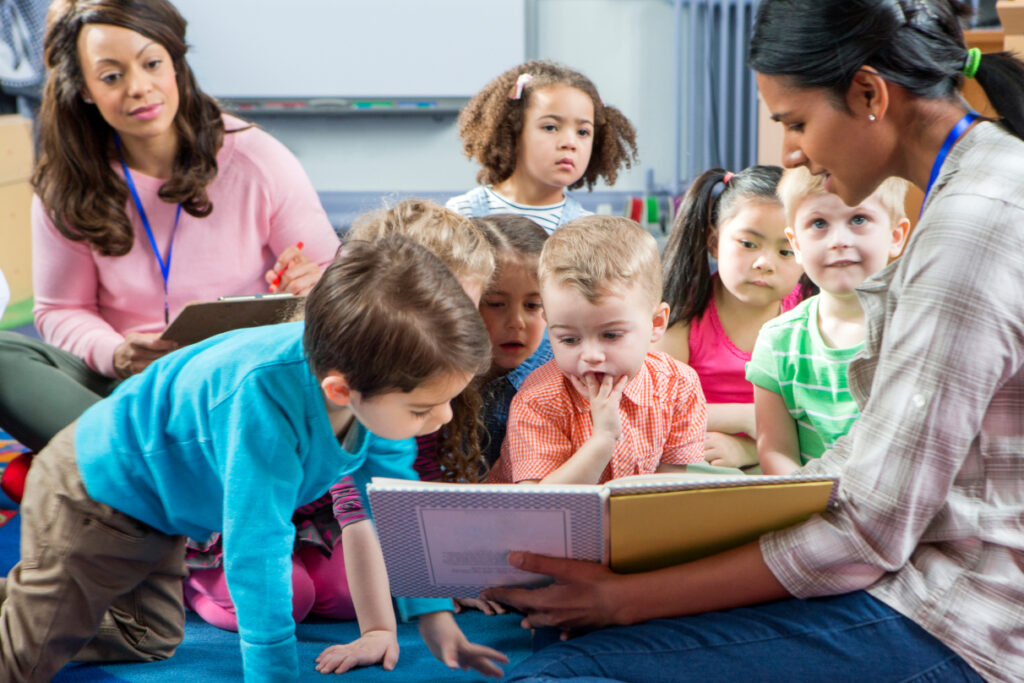 An early years practitioner reads to a group of very interested children sitting on the floor